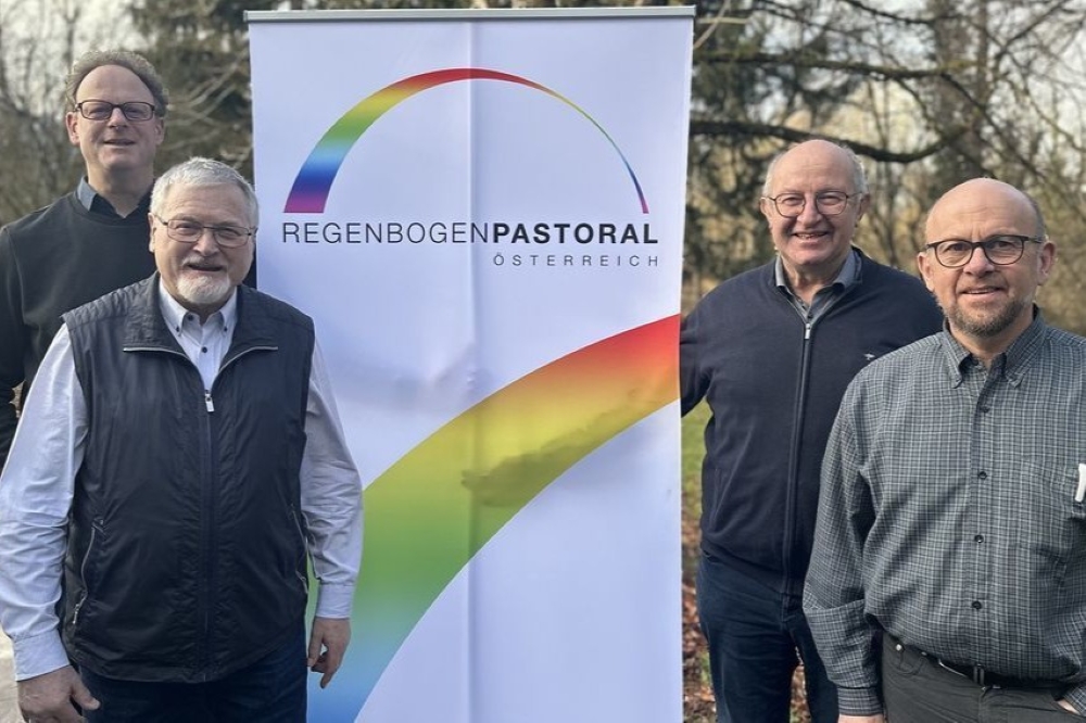 Mitglieder des Leitungsteams der Regenbogenpastoral Österreich vor dem Rollup mit dem Logo