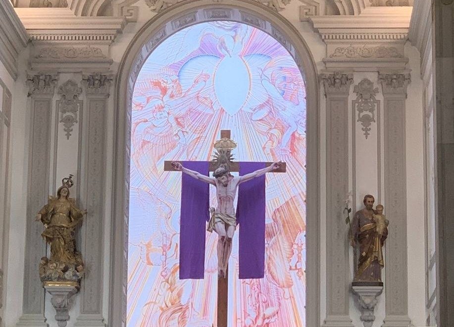 Ein mit einem violetten Tuch verhängtes Kreuz in einer Kirche vor erstrahlendem Hintergrund