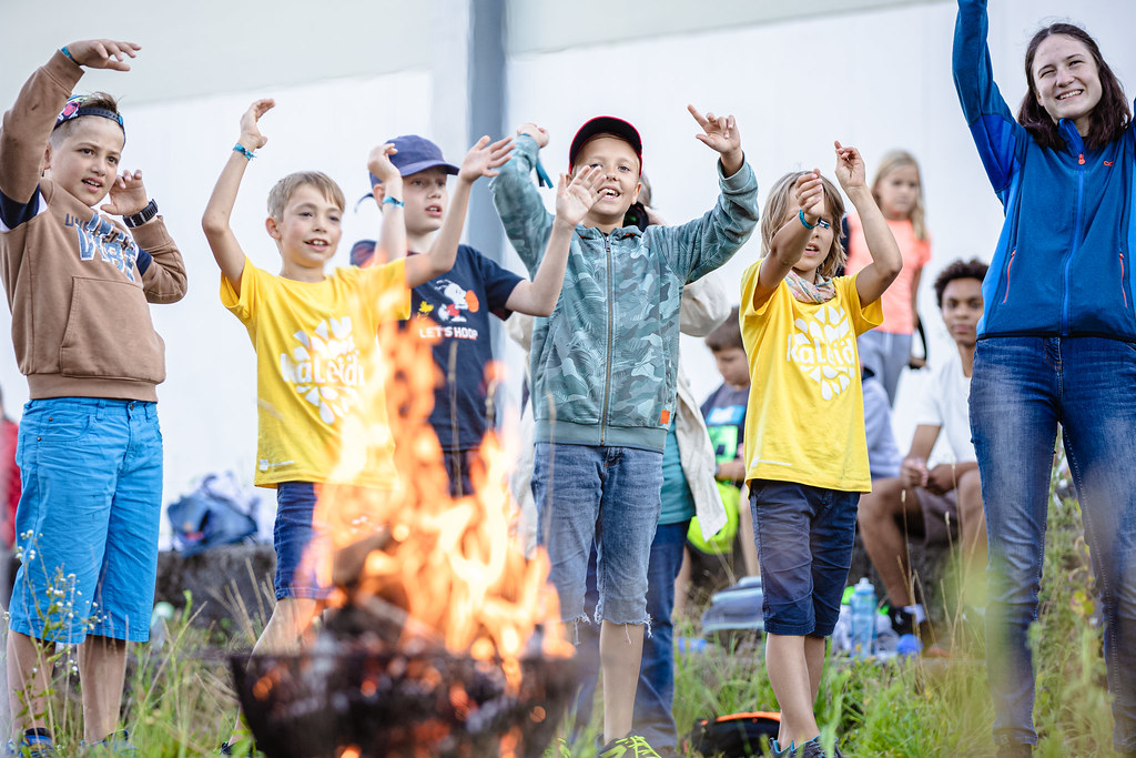 Lagerfeuer und Gruppe von Kindern mit erhobenen Händen