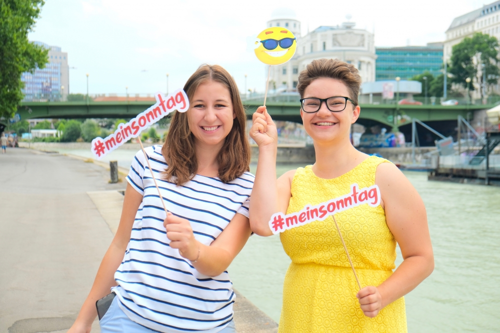 Zwei Frauen stehen am Donaukanal und halten Fähnchen mit der Aufschrift #meinsonntag
