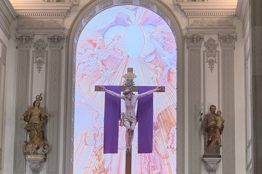 Ein mit einem violetten Tuch verhängtes Kreuz in einer Kirche vor erstrahlendem Hintergrund