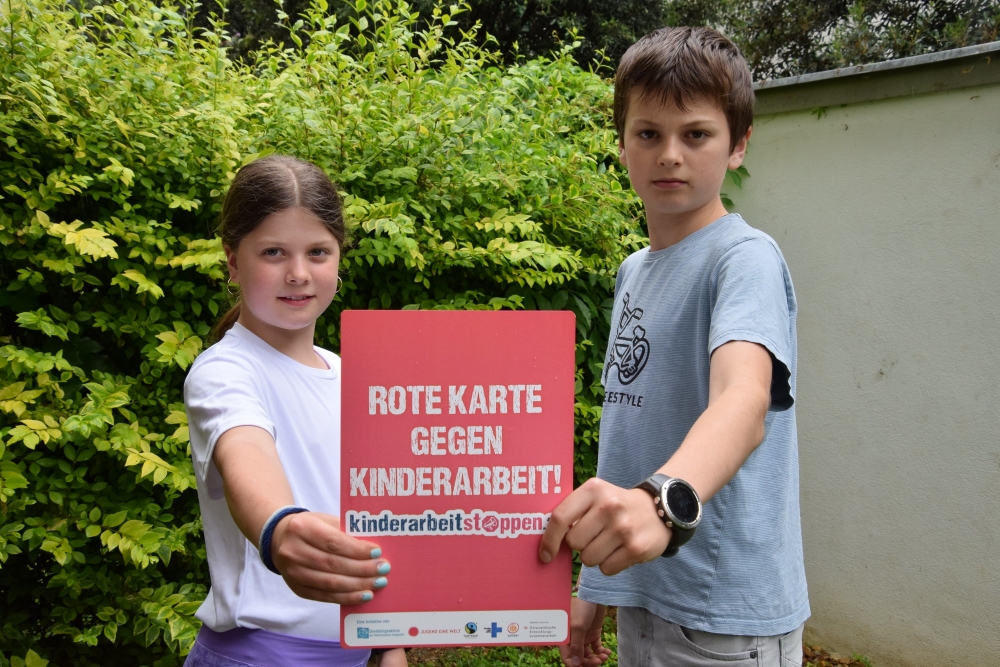 Rote Karte gegen Kinderarbeit / Dreikönigsaktion der Katholischen Jungschar Ein Mädchen und ein Bub halten in den Händen die rote Karte mit der Aufschrift Kinderarbeit Stoppen!