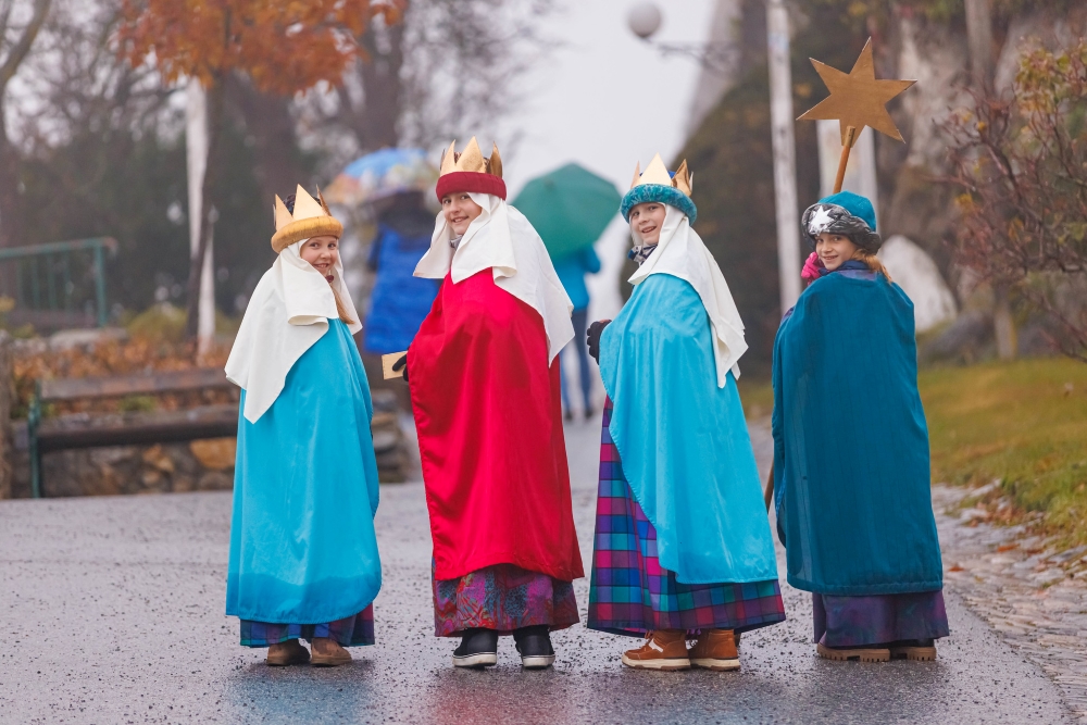 vier junge Menschen verkleidet als König:innen gehen auf der Straße aufwärts und blicken zurück