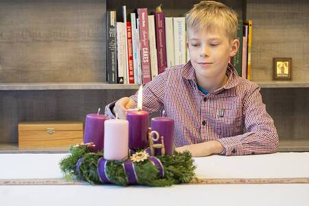 Erster Adventsonntag, ein Junge entzündet am Adventkranz die erste Kerze