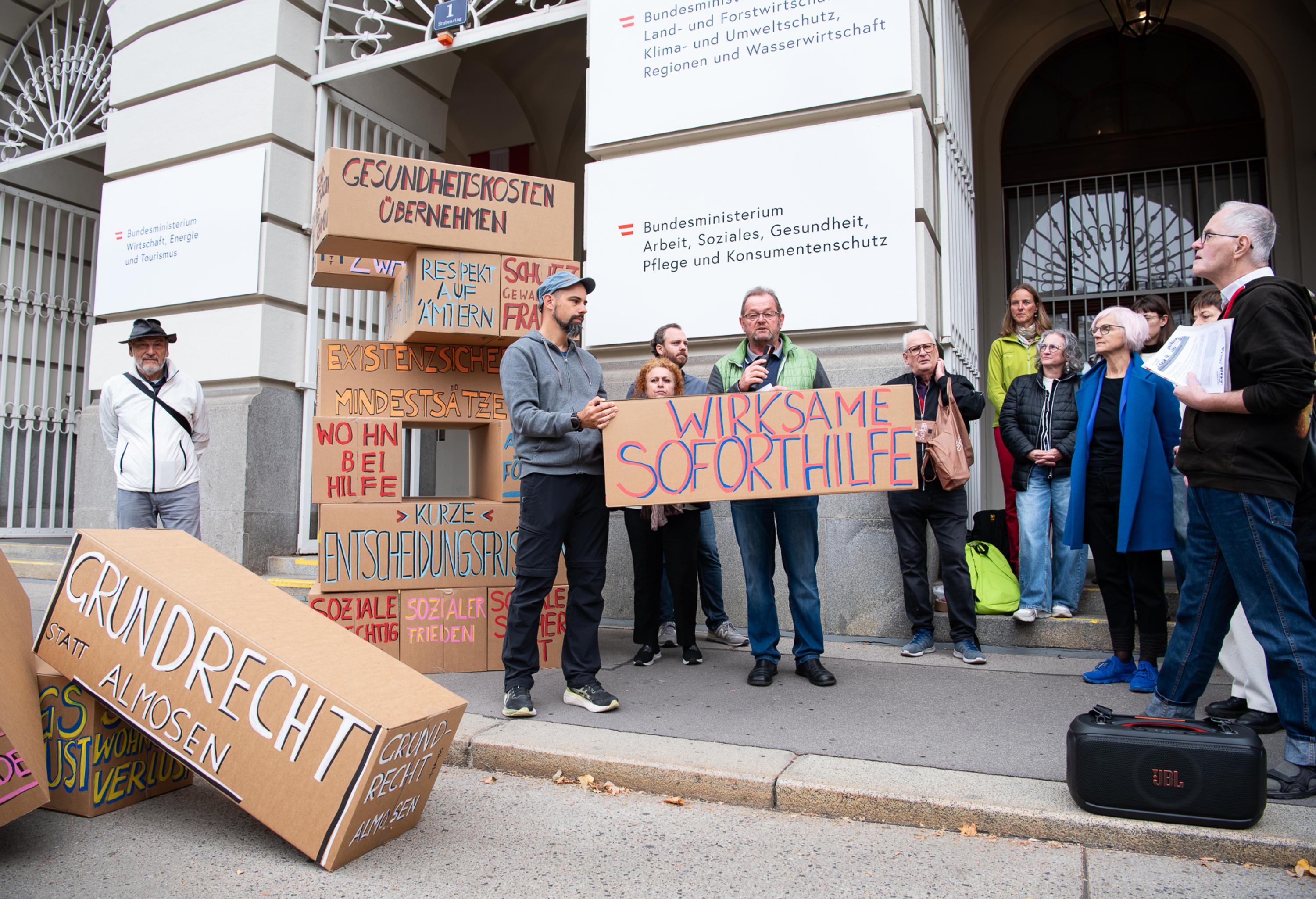KAÖ Präsident Kaineder steht mit einer Gruppe der Armutskonferenz vor dem Sozialministerium und hält ein Statement