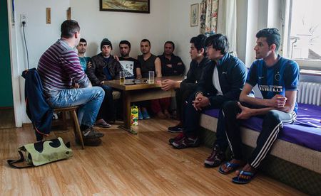Flüchtlinge sitzen um Tisch / Caritas
