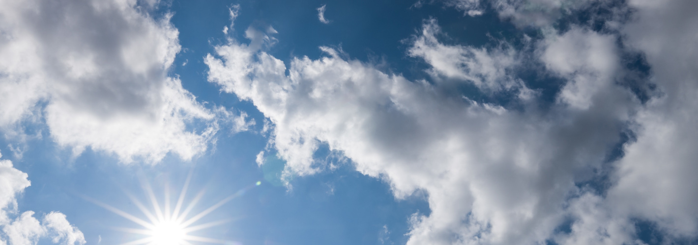 Blauer Hinmmel mit Wolken und Sonne die wärmende Sonnenstrahlen zur Erde sendet.